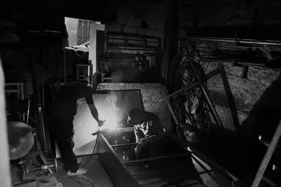 Two people welding in a dimly lit workshop, creating sparks.